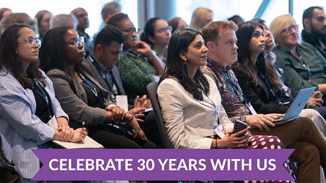 A diverse audience sits attentively in rows at a conference or event, with attendees wearing business attire and lanyards. Many hold notebooks and laptops, appearing engaged and focused. A purple banner at the bottom displays "CELEBRATE 30 YEARS WITH US" in white text, indicating this is an anniversary celebration event.