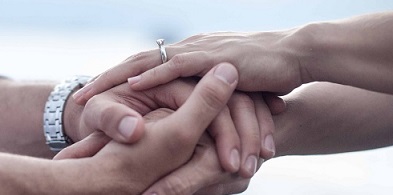 Two pairs of hands with rings are intertwined to represent the bond of marriage