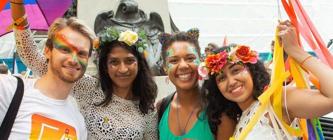 Four people decorated with flowers, face paint and colourful clothes as they celebrate a Pride event. 