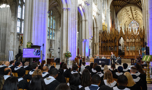 A photo from behind of people wearing black and white gowns facing the front of a large church.