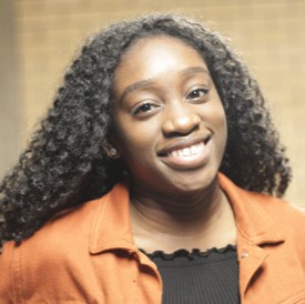 A bright portrait of Dr Makeda Kingue Sousseing smiling wearing an orange shirt over a black top.