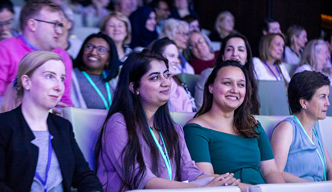 People sitting in a row in an auditorium, talking and smiling. 