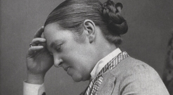 A vintage black and white photo of a woman with one hand up to her forehead in thought.