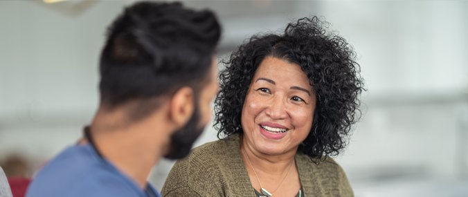 A woman with dark curly hair smiles as a dark-haired man who is facing away from the camera.