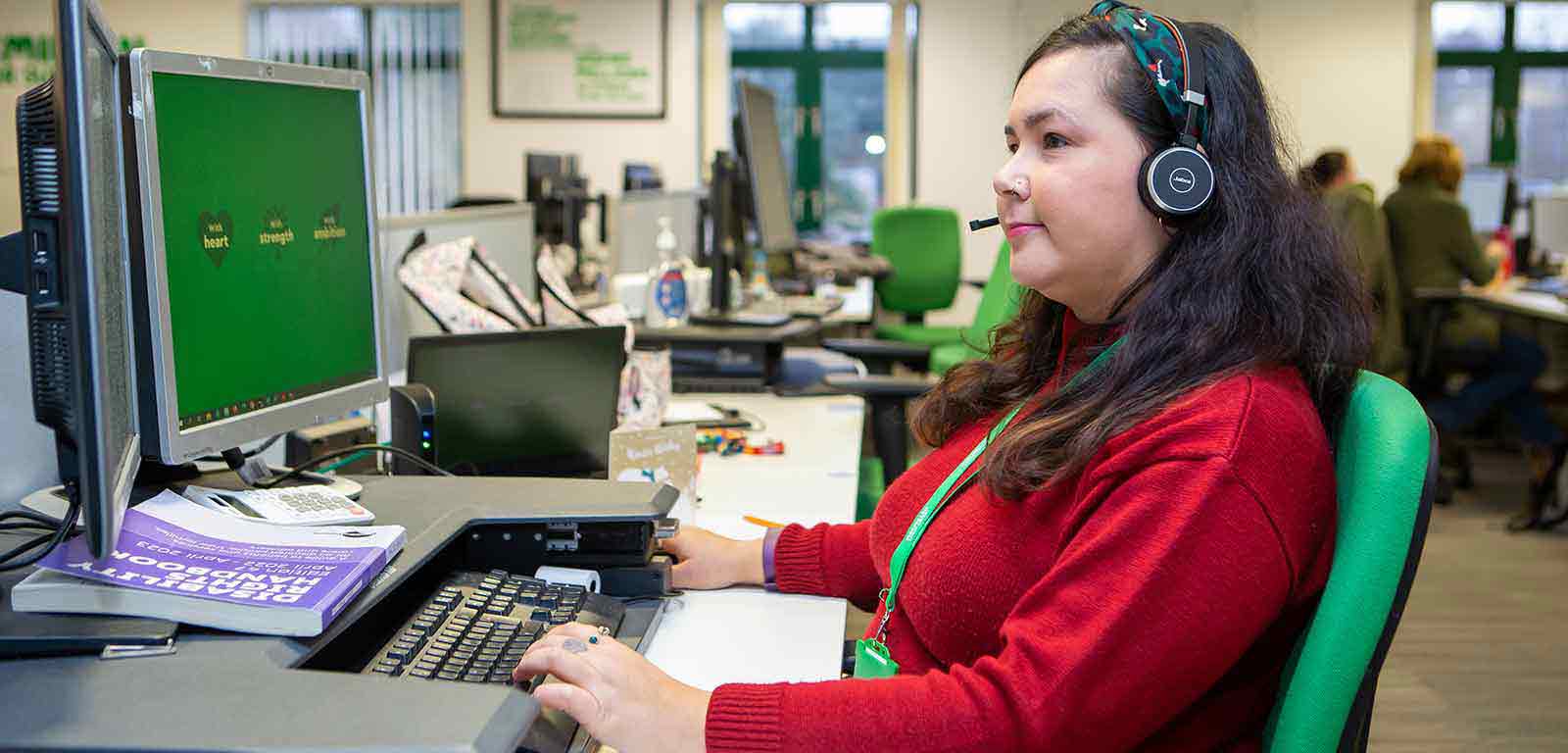 A woman wearing a headset, sitting at a call centre desk