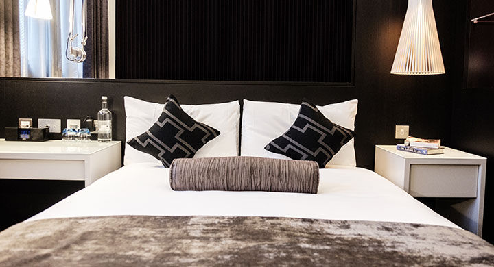 An image of a hotel room with dark walls and white bed sheets.