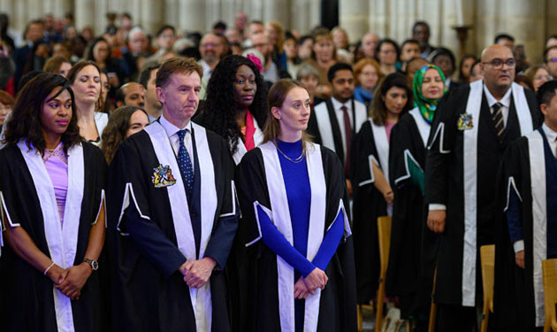 A large crowd wearing ceremonial robes stand from their seats during an event.