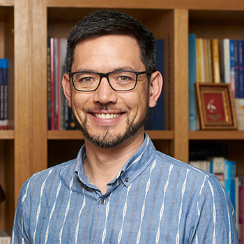 Square photo of Dr Jenichi Dorward, wearing glasses and a blue shirt with white stripes. 
