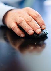A close-up photo of a hand using a mouse with a keyboard in the background. 