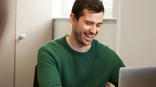 A man wearing a green jumper enjoys a website on a laptop.