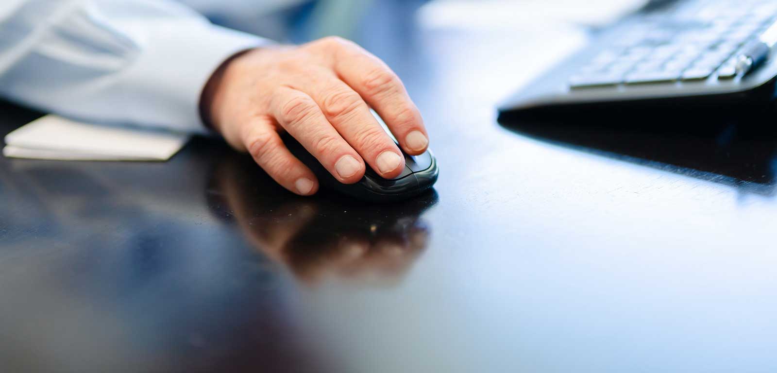 A close-up photo of a hand using a mouse with a keyboard in the background. 