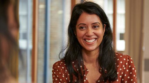 A woman smiling showing her teeth standing next to a man wearing a green jumper also smiling at a woman standing in front of them.