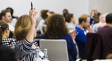 A woman raising her hand to ask a question at a seminar