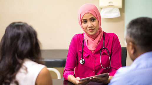 A GP wearing a pink hijab talks with a couple during a GP appointment. 
