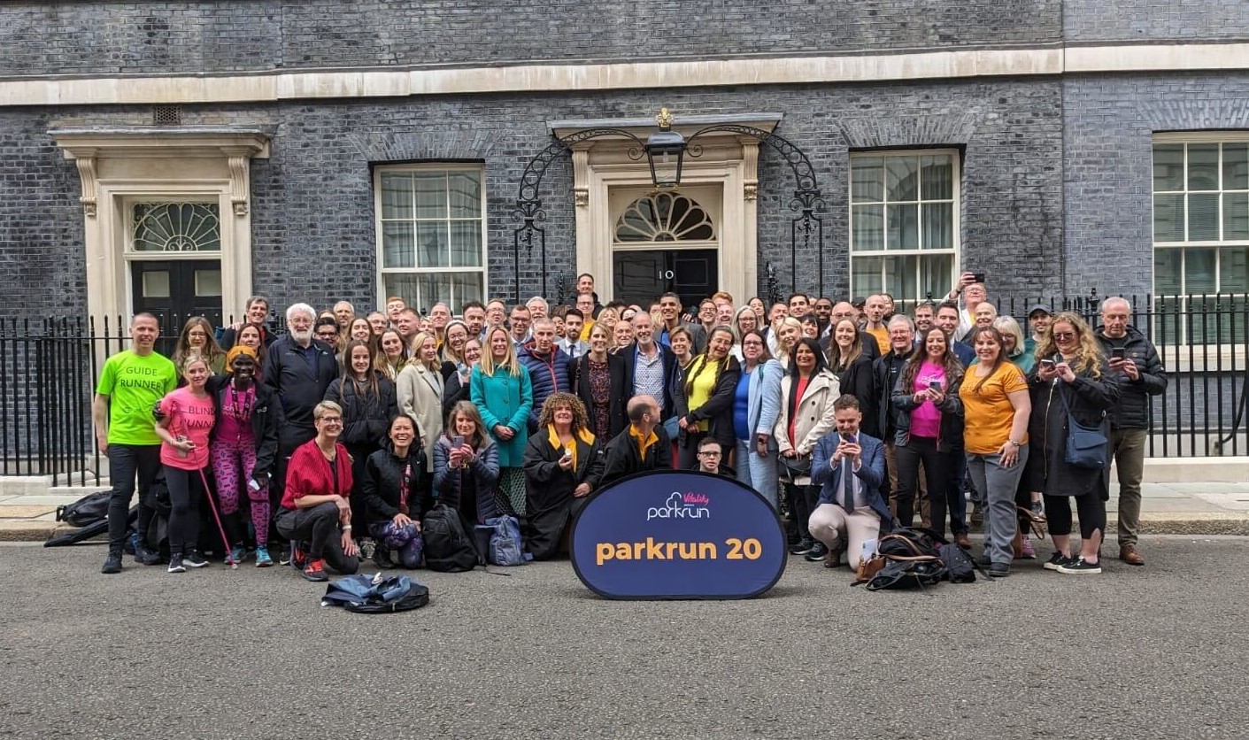 A group of parkrun runners wearing bright clothing smile for a group photo outside 10 Downing Street.