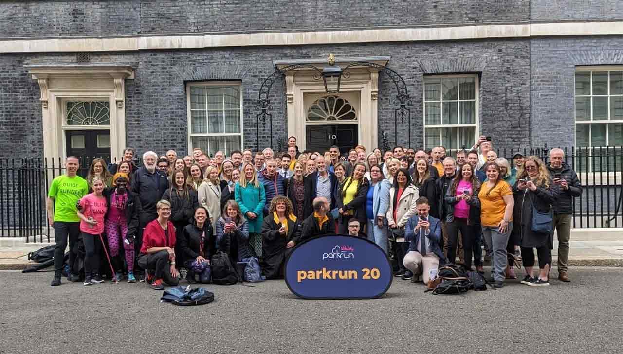 A group of parkrun runners wearing bright clothing smile for a group photo outside 10 Downing Street.