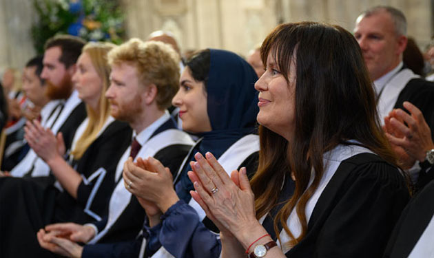 A photo focused on a line of attendees sitting on chairs and clapping an event out of shot.