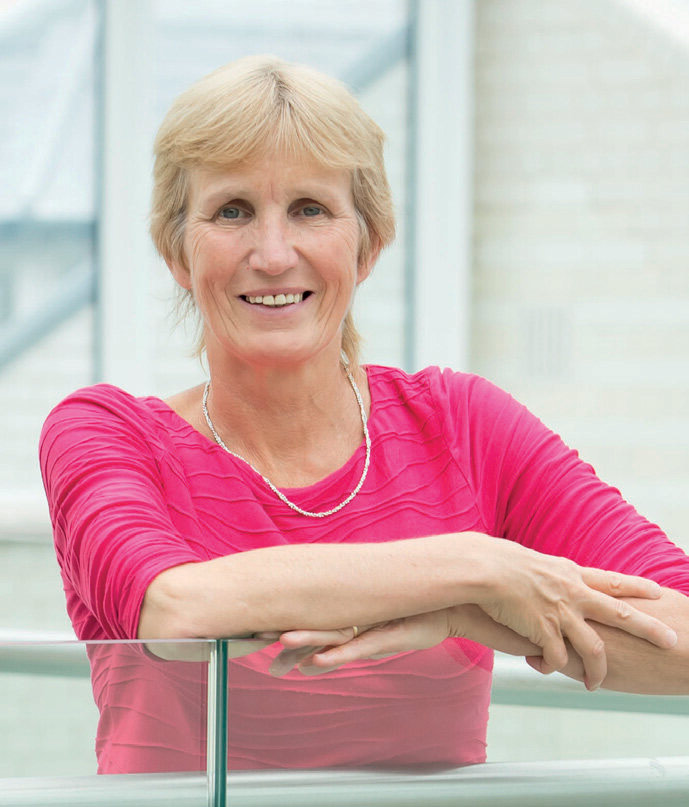 A headshot of Dr Anne Connolly wearing a bright pink top. 