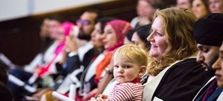A woman sitting in a group at an RCGP members' ceremony with a toddler on her lap
