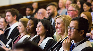 A multicultural seated crowd smile and laugh at a speaker on stage out of shot. 