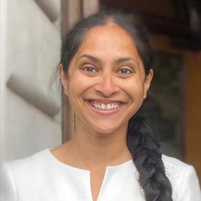 Dr Deepthi Lavu smiles at the camera wearing a white top with her long dark hair in a braid to one side.