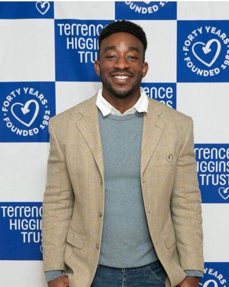 Dr Amos smiling standing against a Terrence Higgins Trust backdrop.