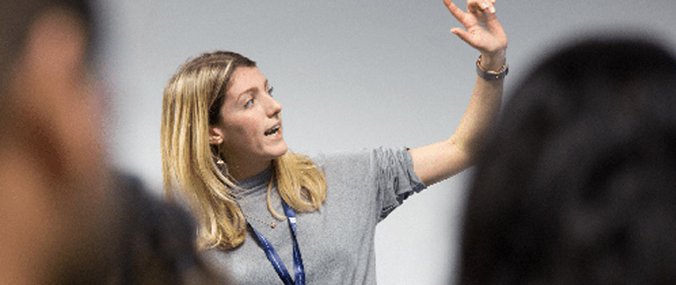 A woman at the front of a crowd raising her arm in conversation.