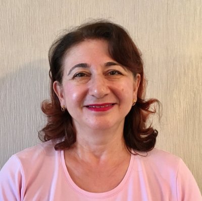 Dr Hastie Salih smiles in front of a cream wall wearing a light pink t-shirt. 