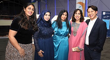 A group of five people of different heritage smile for the camera at an evening event
