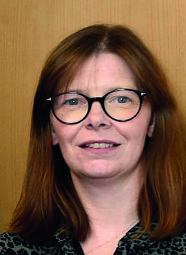 A close-up photo of Dr Ursula Mason standing in front of a wooden background. 