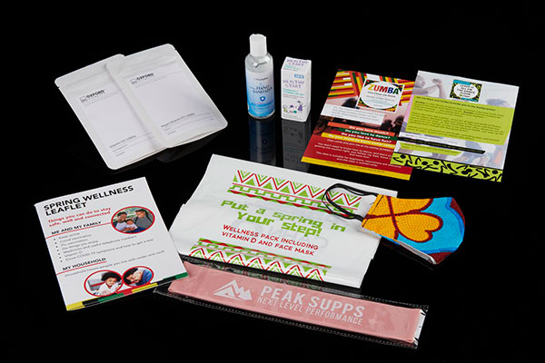 COVID-19 health pack with vitamins, hand sanitiser, face mask, leaflets, and exercise band on a black background