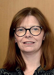 A close-up photo of Dr Ursula Mason standing in front of a wooden background.
