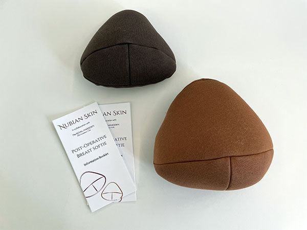Two post-operative breast softies in dark brown and medium brown shades, with two Nubian Skin information booklets on a light surface.