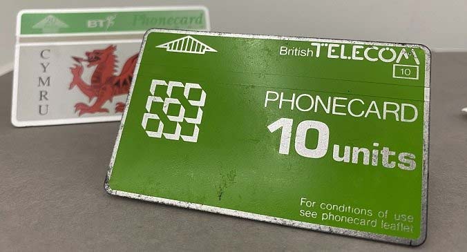 A green BT phone card, reading: British Telecom, Phonecard, 10 units, for conditions of use see phonecard overleaf. Behind is another phonecard, out of focus, with the Welsh red dragon and the word Cymru on it.